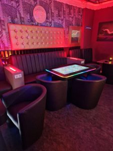 Gemütliche Lounge mit Spieltisch und bequemen Sesseln in stilvollem Ambiente bei Neonlicht.