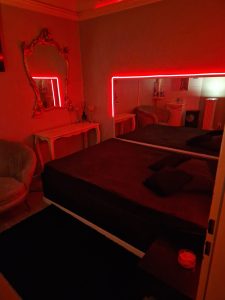 Gemütliches Schlafzimmer mit roter LED-Beleuchtung, Spiegel, Vintage-Möbeln und entspanntem Ambiente.
